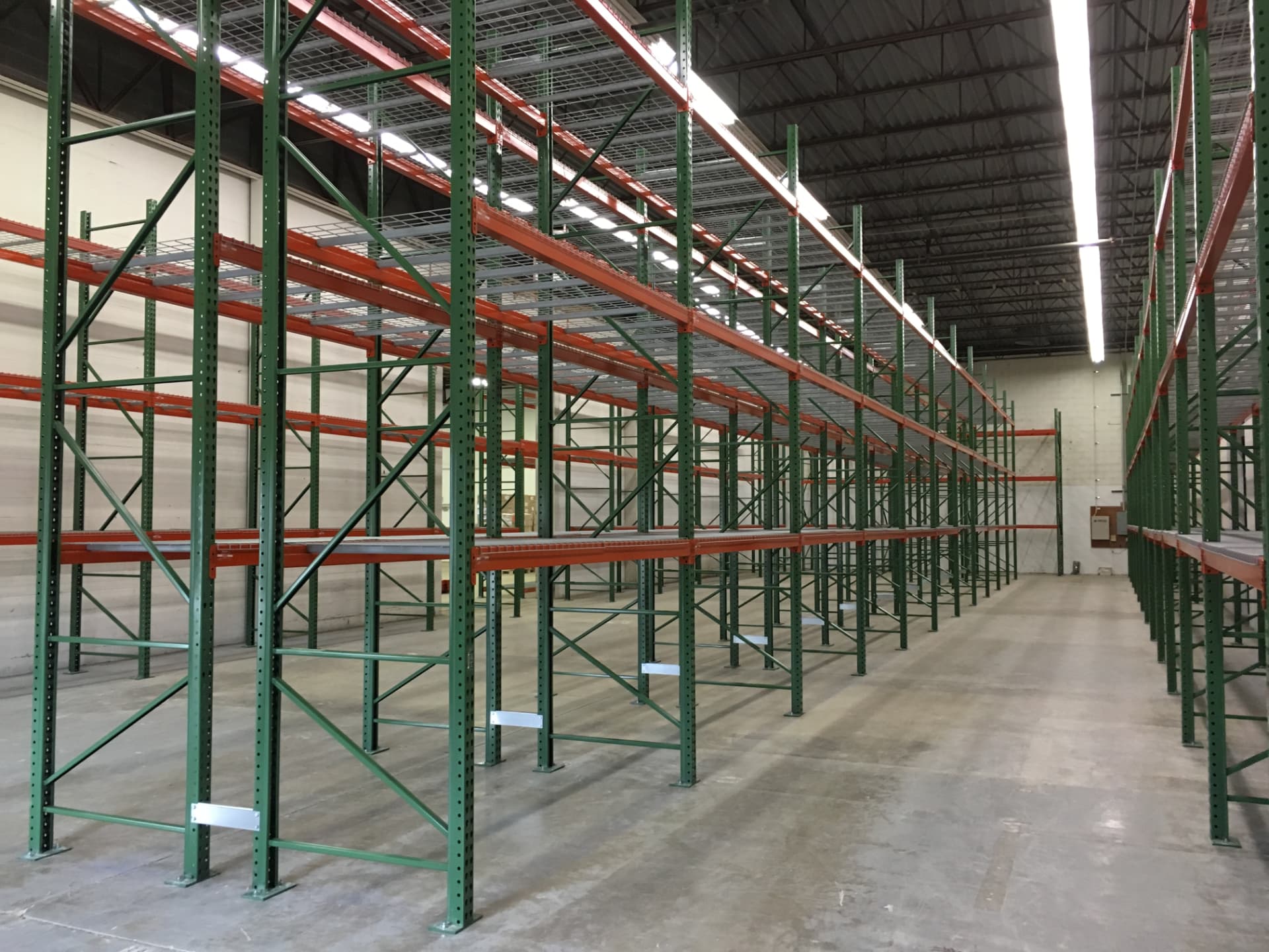 Green and orange selective pallet rack rows along a warehouse wall